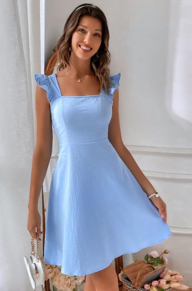 une femme en robe courte dos nu couleur bleue evangeline posant devant un fond neutre avec un sourire radieux