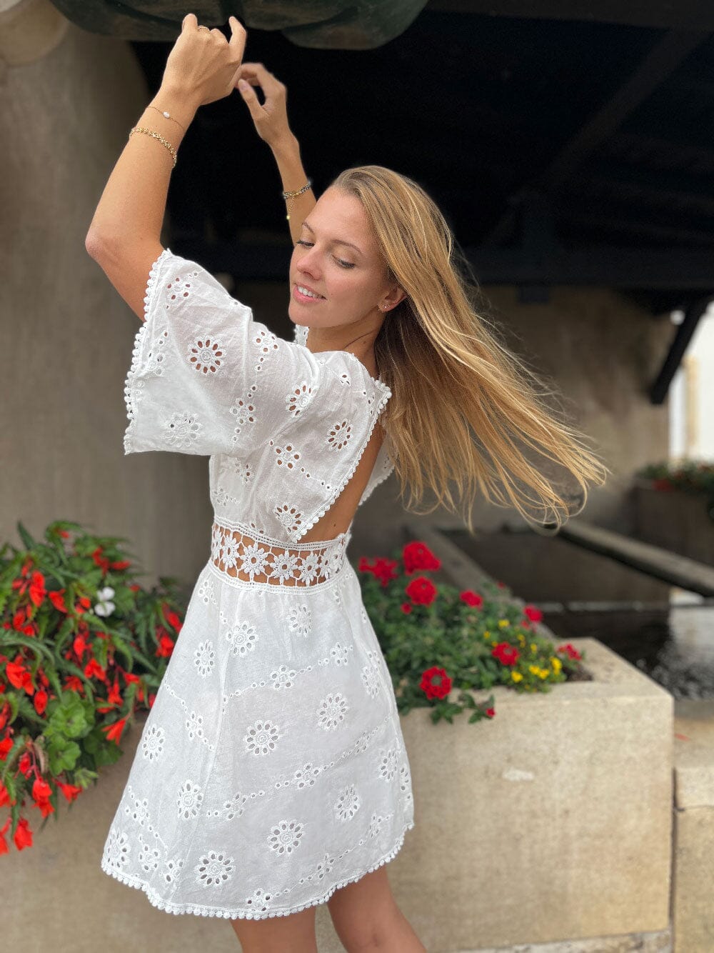 Robe bohème dos nu en dentelle blanche, parfaite pour l'été, avec détails floraux, portée dans un jardin fleuri.