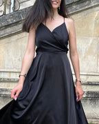Robe satin élégante noire mi-longue avec bretelles fines, idéale pour une soirée chic et féminine en extérieur.