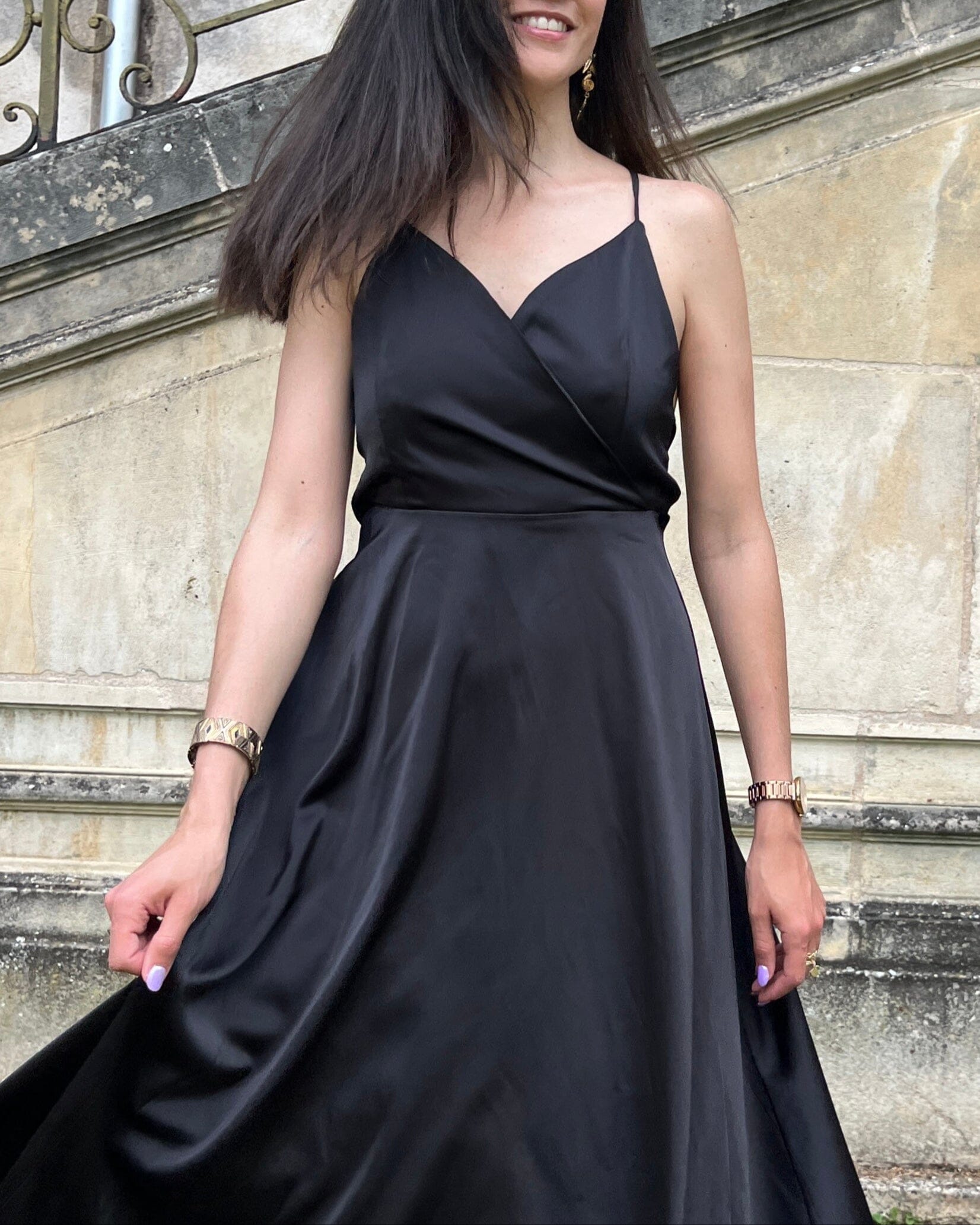 Robe satin élégante noire mi-longue avec bretelles fines, idéale pour une soirée chic et féminine en extérieur.