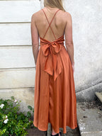 Robe en satin mi-longue couleur terre cuite avec dos nu et bretelles croisées, style élégant et chic parfaite pour l'été.
